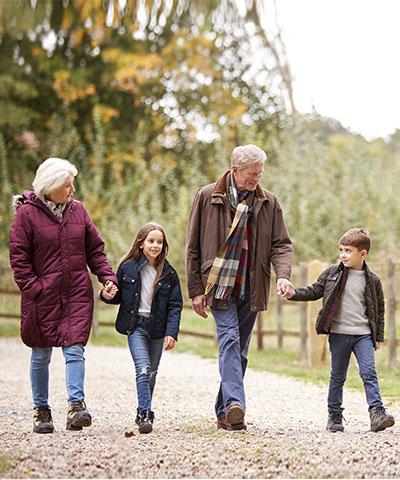 Ventajas para particulares - Abuelos con los nietos sonriendo mientras que caminan por el campo rodeados de árboles Ventajas para particulares - Abuelos con los nietos sonriendo mientras que caminan por el campo rodeados de árboles