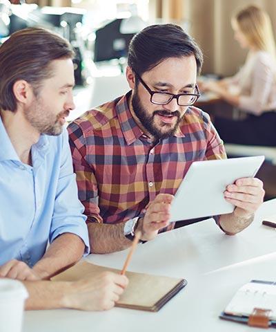 Seguros Colectivos para Empleados - Dos trabajadores con camisa trabajando en la oficina con su tablet Seguros Colectivos para Empleados - Dos trabajadores con camisa trabajando en la oficina con su tablet
