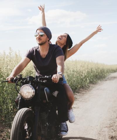 Seguro del Automóvil - Pareja joven feliz en su moto conduciendo por un camino Seguro del Automóvil - Pareja joven feliz en su moto conduciendo por un camino