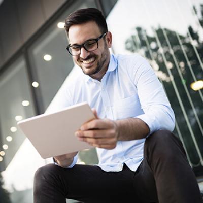 Informe de carteras - Hombre joven con gafas y camisa blanca sentado en la oficina con su tablet viendo informes de mercados Informe de carteras - Hombre joven con gafas y camisa blanca sentado en la oficina con su tablet viendo informes de mercados