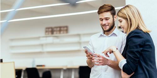 Promocion Asesoramiento especializado - Perosnas de negocios sonriendo con el movil en la mano mirando la app de ruralvia mi negocio en la oficina